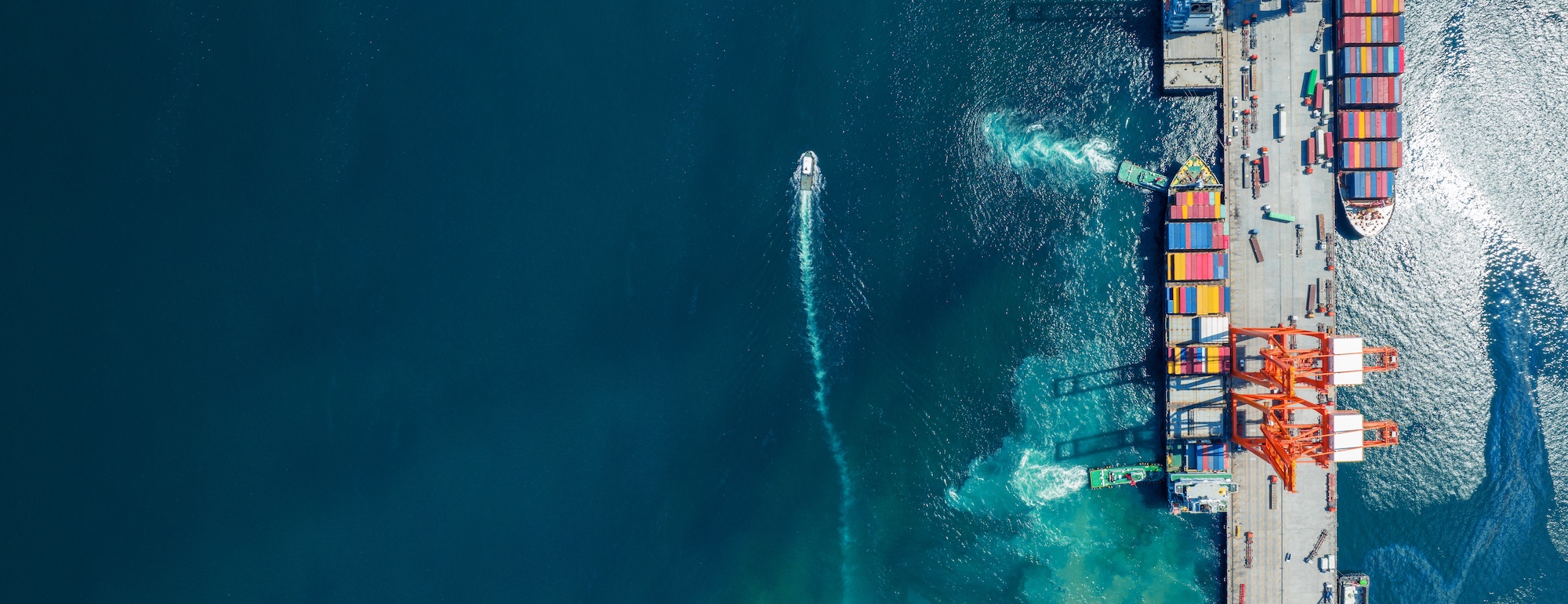 Two cargo container ships docked under a crane and seen from above.