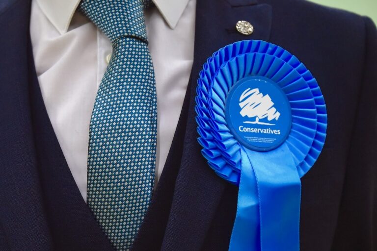 A close up of a Conservative Party rosette on the lapel of a suit jacket.