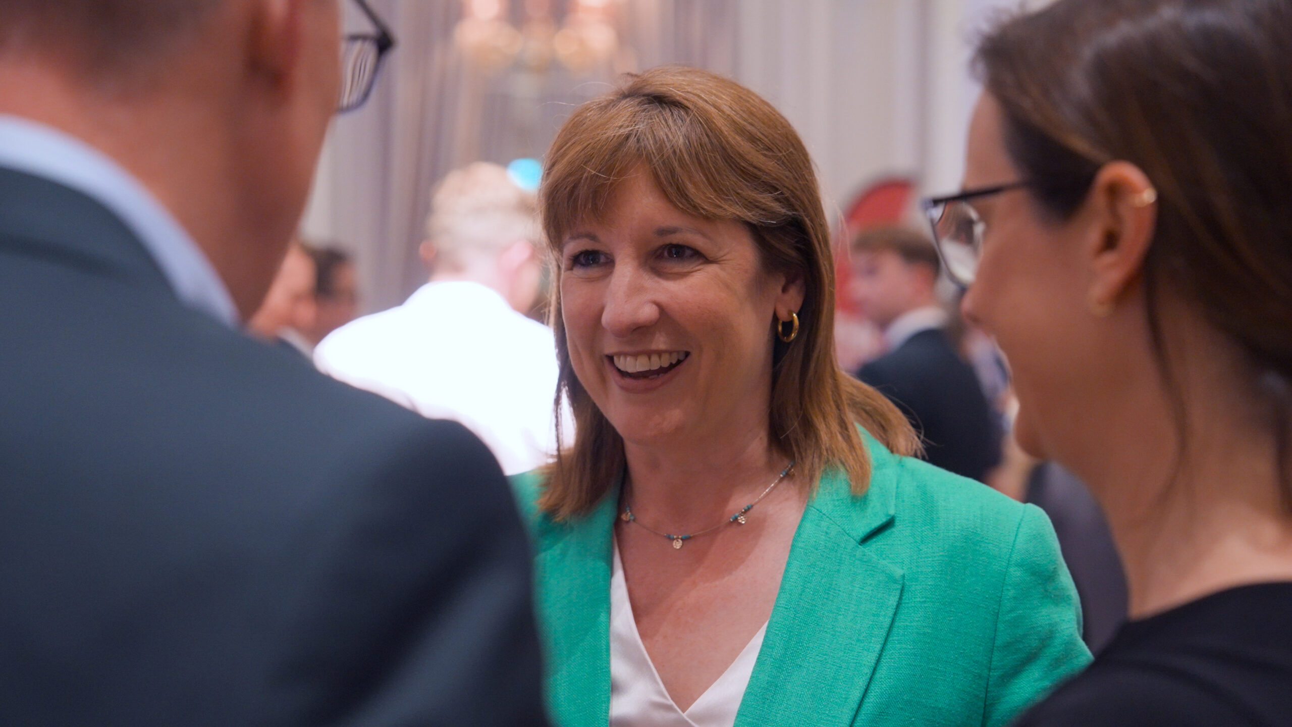 Chancellor of the Exchequer, Rt Hon Rachel Reeves MP, speaks to guests at Arden Strategies's summer reception at the Corinthia Hotel in Whitehall, London. She wears a green blazer and white blouse, and is facing the camera and smiling. A man and a woman in dark office wear face her.