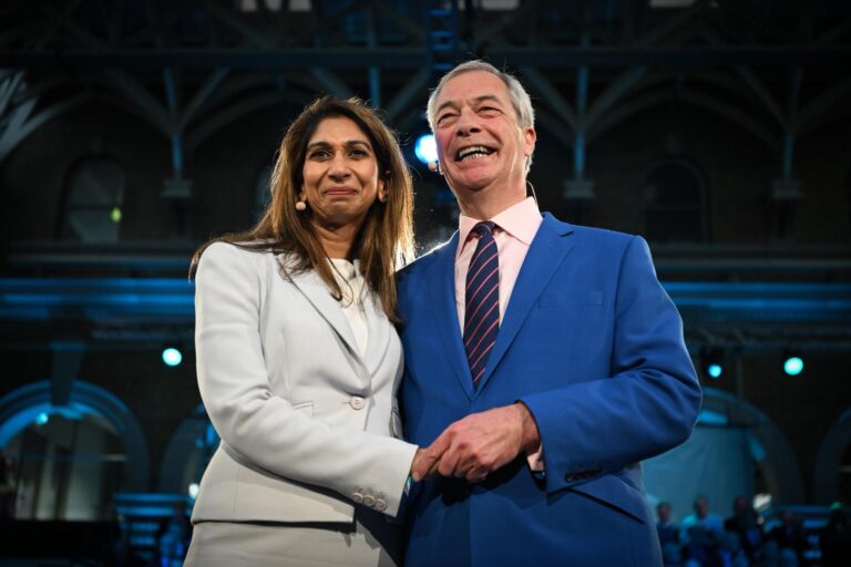Suella Braverman and Nigel Farage in formal attire stand close together, smiling, on a stage with an arched architectural backdrop as the former Home Secretary was unveiled as the latest Conservative MP to defect to Reform UK at an event in London.